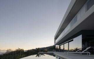 Moderna kuća s velikim prozorima i ležaljkama pored infinity bazena, s pogledom na krajolik u zalazak sunca. Elko - Instalacija Pametnih Kuća i Smart Home Sistema