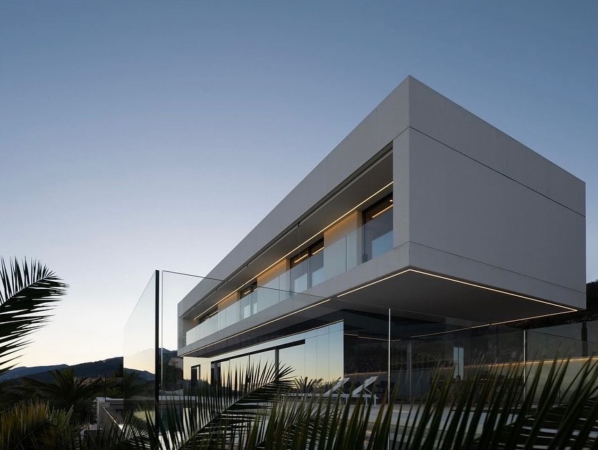 Moderna dvokatnica s velikim staklenim prozorima, čistim linijama i minimalističkim dizajnom, okružena palmama, fotografirana u sumrak. Elko – Instalacija Pametnih Kuća i Smart Home Sistema Moderna dvokatnica s velikim staklenim prozorima, čistim linijama i minimalističkim dizajnom, okružena palmama, fotografirana u sumrak. Elko - Instalacija Pametnih Kuća i Smart Home Sistema