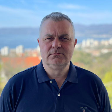 Muškarac srednjih godina s kratkom sijedom kosom u mornarsko plavoj polo majici stoji vani s mutnim gradskim pejzažem i planinama u pozadini. Elko – Instalacija Pametnih Kuća i Smart Home Sistema Muškarac srednjih godina s kratkom sijedom kosom u mornarsko plavoj polo majici stoji vani s mutnim gradskim pejzažem i planinama u pozadini. Elko - Instalacija Pametnih Kuća i Smart Home Sistema